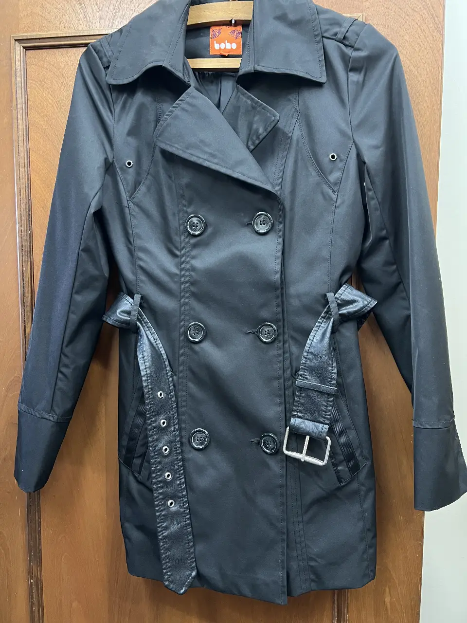 Trench negro de mujer, con doble botonadura, cinturón y detalles de diseño. Ideal para un look elegante y sofisticado.