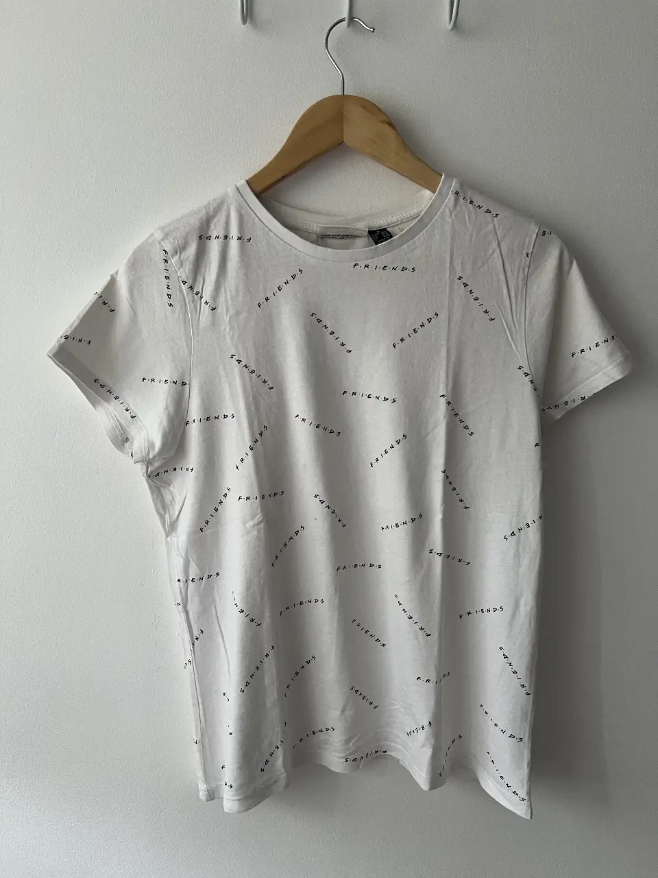 Remera de manga corta blanca con estampado repetido de la palabra "FRIENDS" en negro. Ideal para un look casual y cómodo.