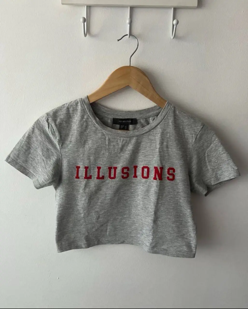 Remera crop gris con estampado "ILLUSIONS" en rojo. Ideal para un look casual y moderno.