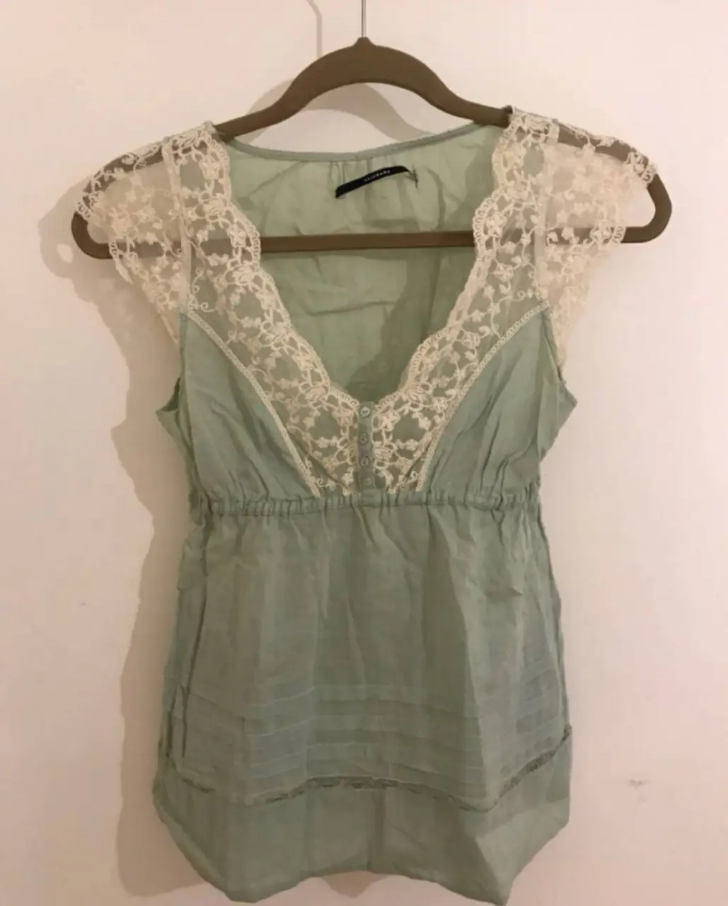 Blusa de mujer color verde agua con detalles de encaje en el cuello y mangas. Tiene un corte holgado y un elástico en la cintura para un ajuste cómodo. Ideal para un look fresco y femenino.