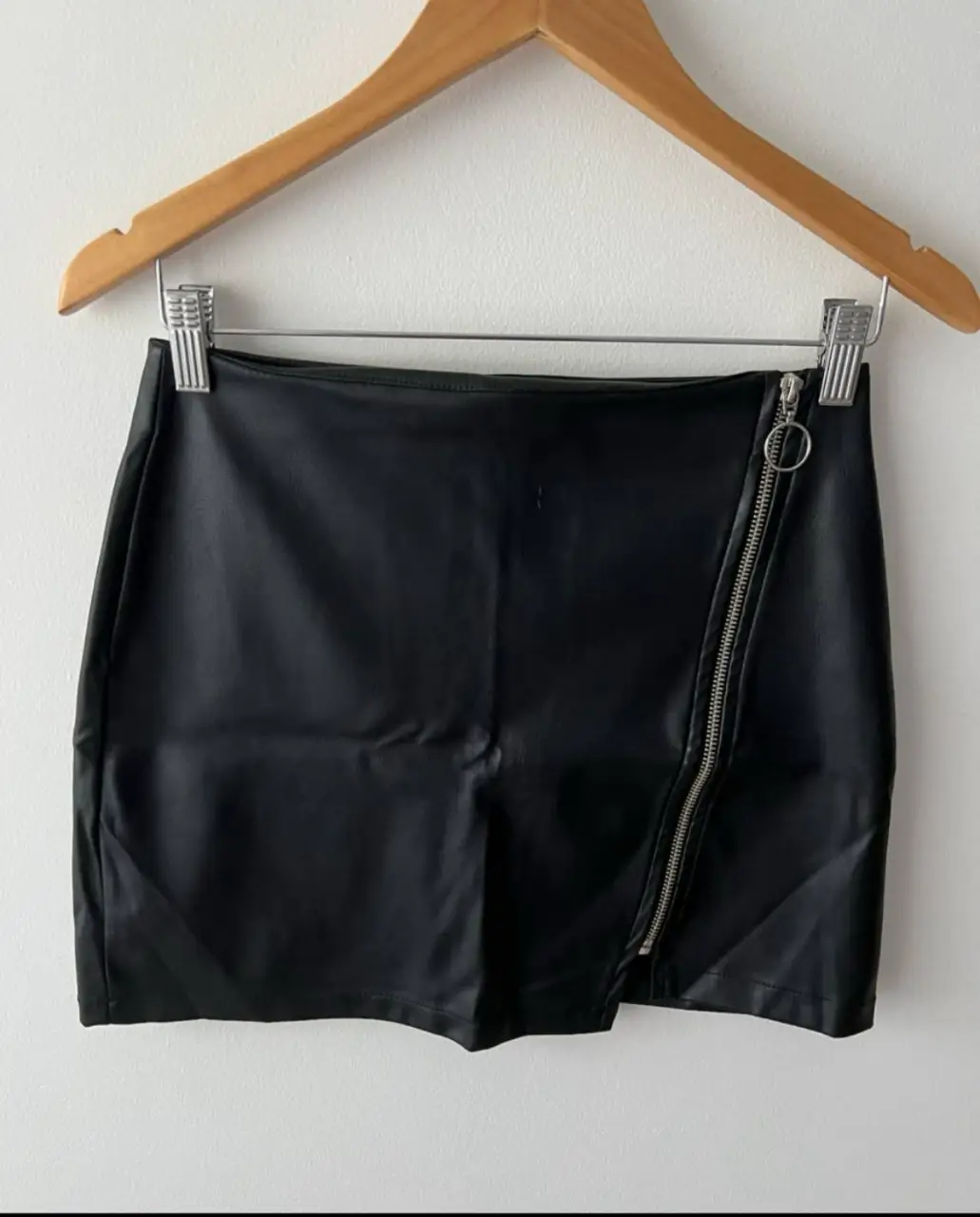Minifalda de cuero sintético negra con cierre diagonal y detalle de argolla. El único detalle que tiene es que está un poco rasgado en la parte de adelante (cuarta foto). Ideal para un look moderno y audaz.