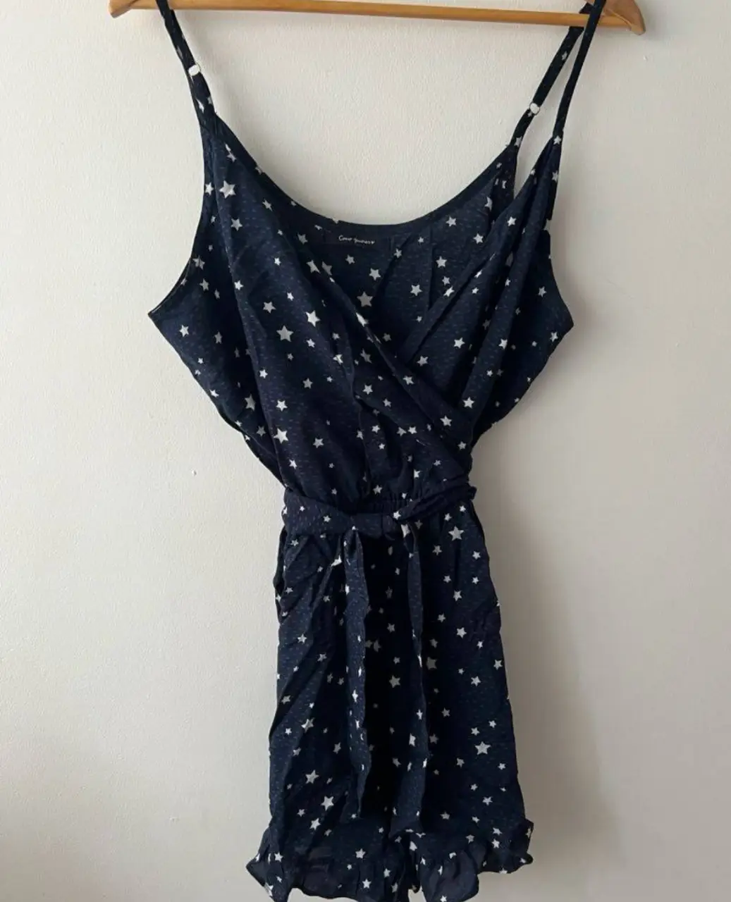 Mono corto de mujer, con estampado de estrellas blancas sobre fondo azul oscuro. Tiene un diseño envolvente con cinturón para ajustar la cintura y volados en el borde inferior. Ideal para un look fresco y casual.