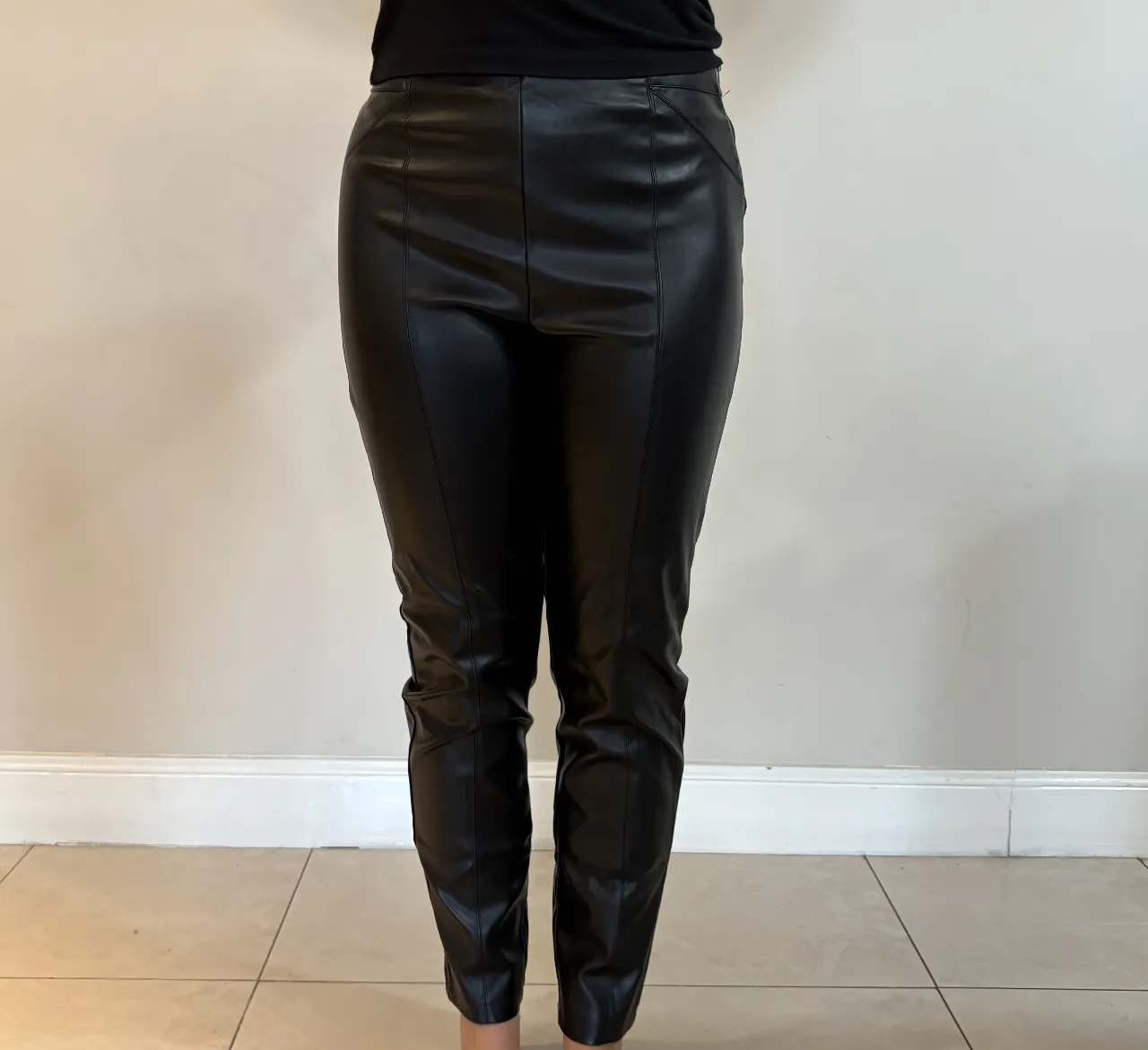 Pantalon de cuero negro tiro alto, con costuras que realzan la figura. Un básico versátil para looks de día o de noche.