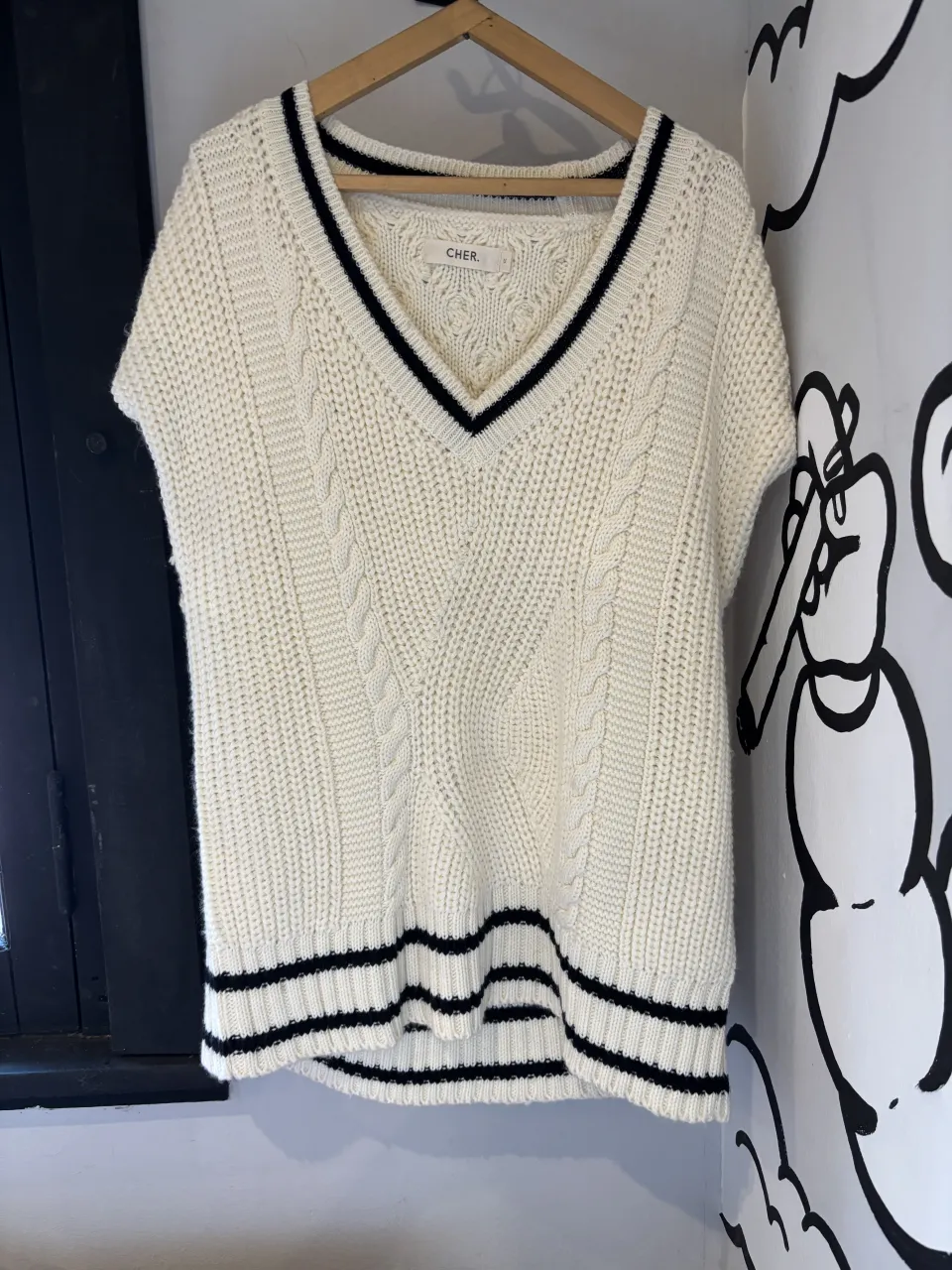 Sweater de tejido de punto con cuello V y detalles de rayas. Diseño sin mangas con trenzas en el frente y espalda. Ideal para un look casual y moderno.