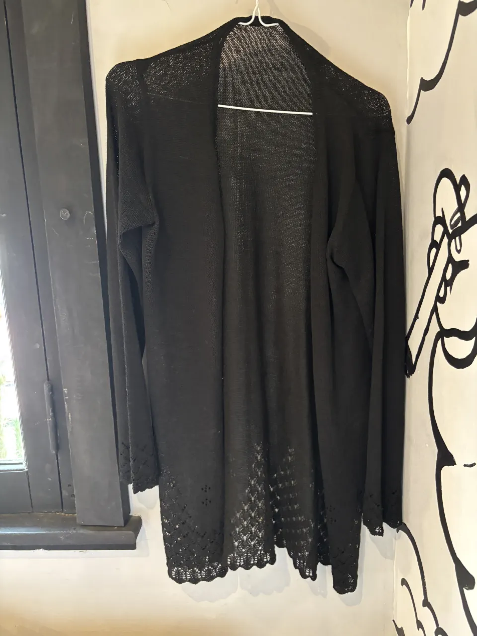 Cardigan negro largo, tejido con detalles de puntilla en los puños y en el borde inferior. Ideal para un look casual o elegante.