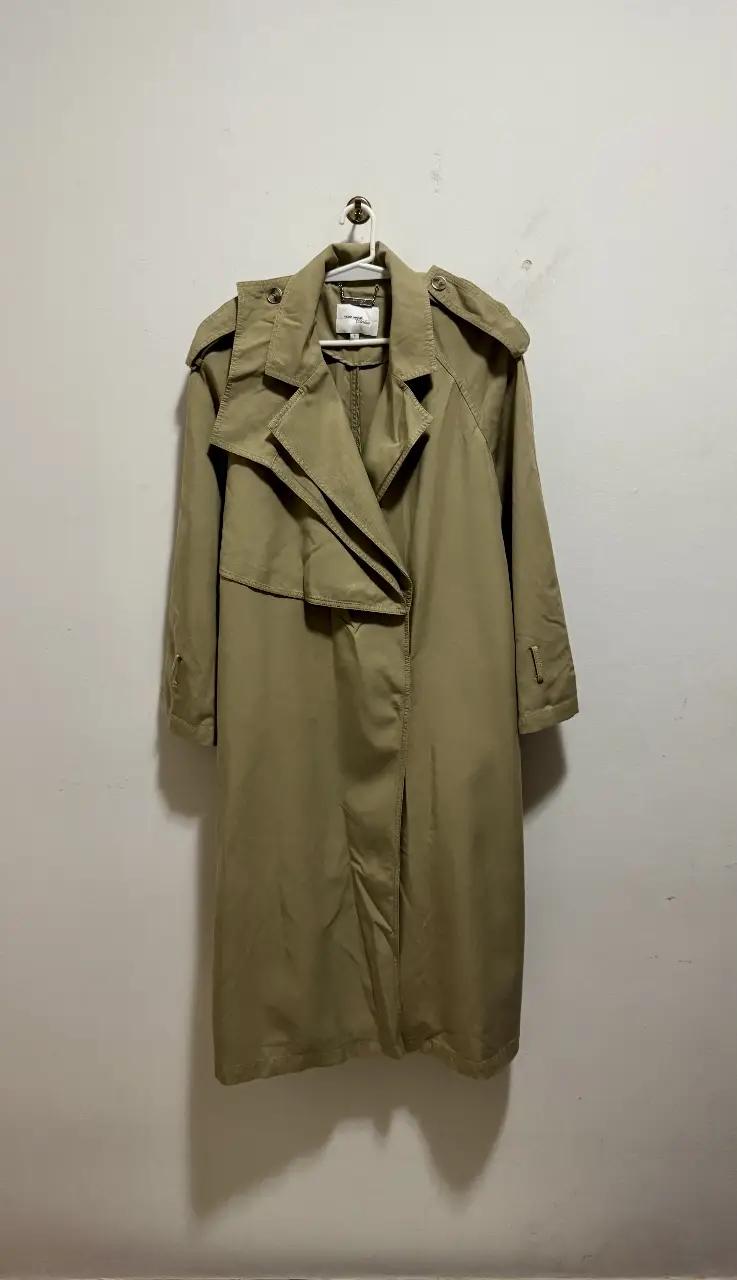 Trench coat clásico de color verde militar claro, ideal para el entretiempo. Confeccionado en tela resistente, este trench presenta un diseño atemporal con solapas amplias, y detalles funcionales. Perfecto para un look elegante y versátil.