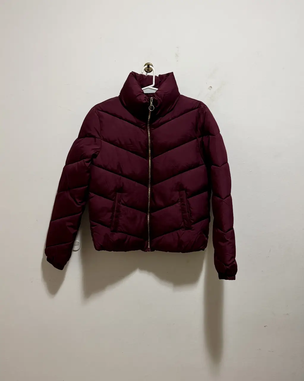 Campera de pluma acolchada color borgoña con cuello alto y cierre. Ideal para el invierno.