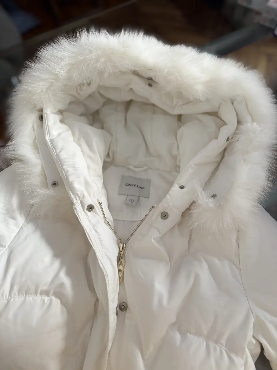 Campera de pluma blanca con capucha y borde de piel sintética. Ideal para el invierno, abrigada y con cierre. Perfecta para un look casual y cómodo.