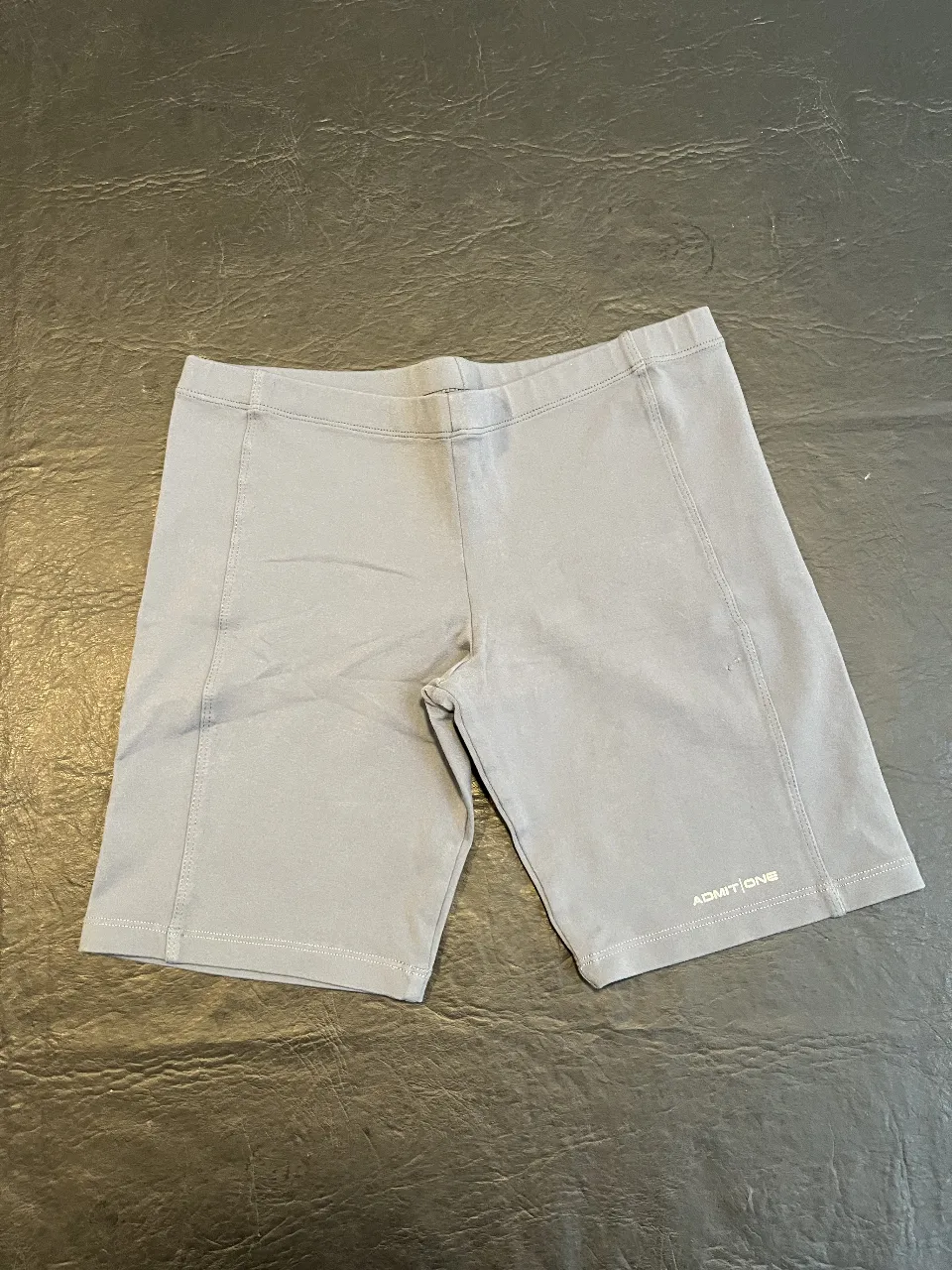 Short deportivo gris de la marca Admit One, ideal para actividades físicas. Confeccionado en tela elastizada para mayor comodidad y libertad de movimiento. Perfecto para tus entrenamientos.