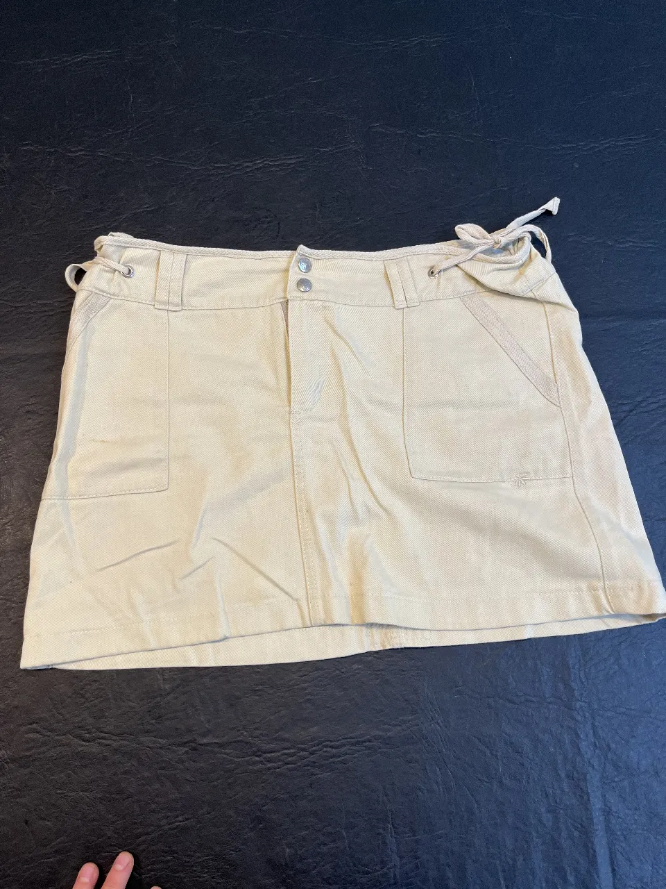 Pollera de gabardina color crudo, con bolsillos delanteros y traseros. Detalles de ajuste en la cintura y un diseño versátil para diversas ocasiones.