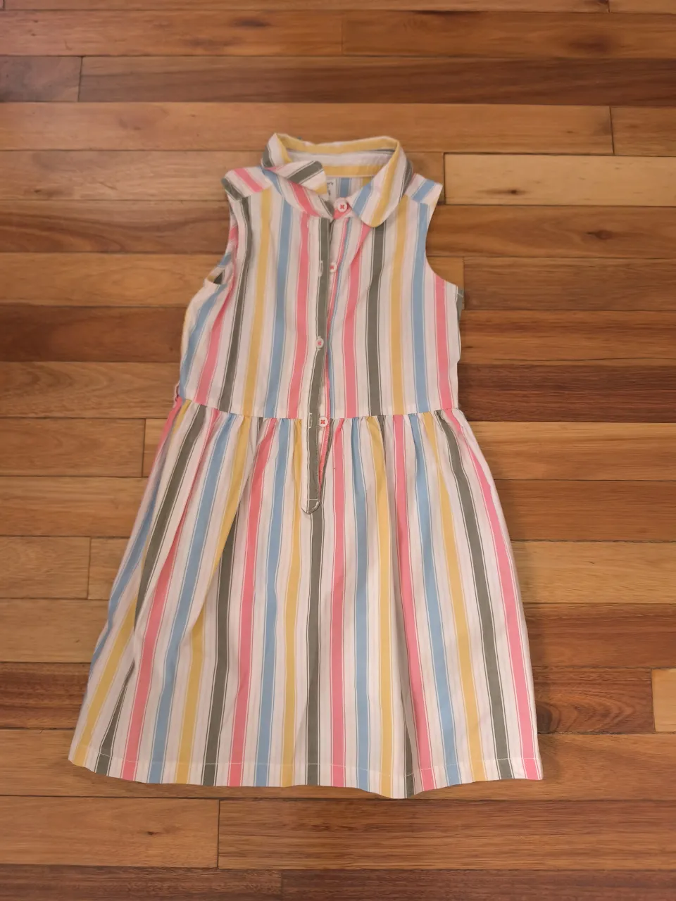 Vestido a rayas multicolor, ideal para niñas. Con cuello camisero y botones al frente, tiene un corte a la cintura con elástico y falda con caída. Perfecto para el día a día o salidas casuales en días cálidos.
