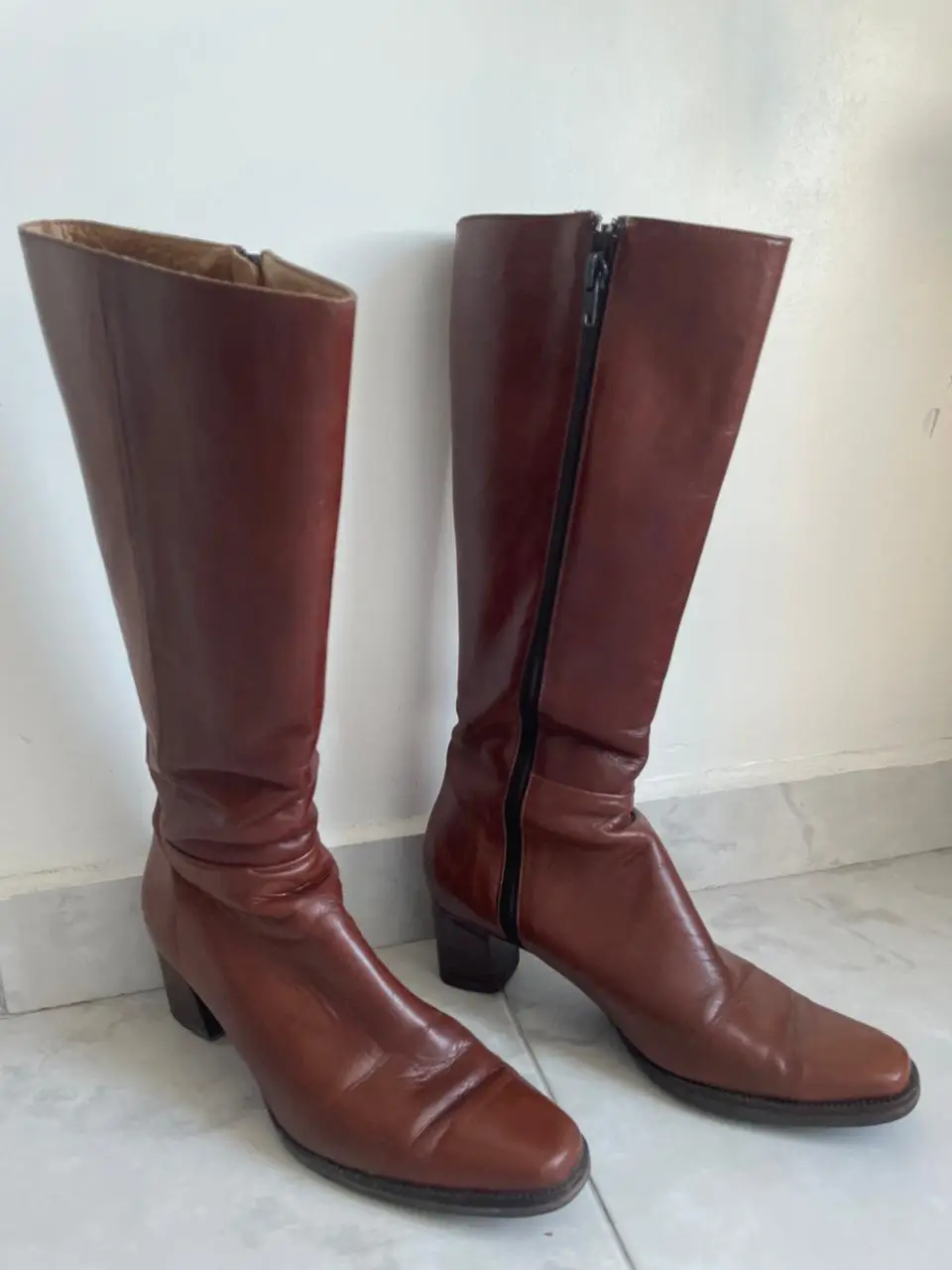 Botas de caña alta de cuero marrón, con cierre lateral y taco bajo. Ideales para un look retro y elegante.