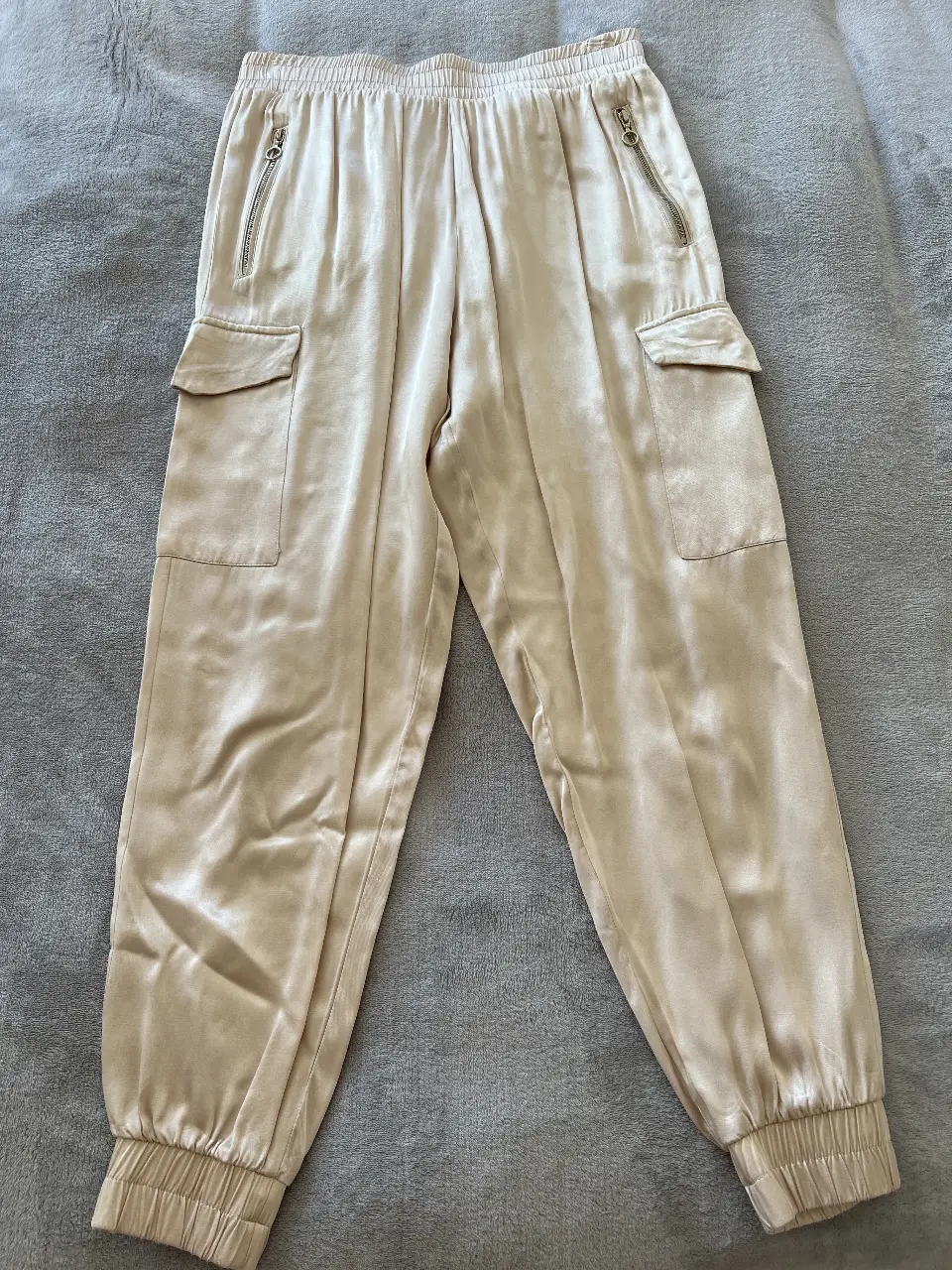 Pantalón babucha de satén color crudo, con bolsillos laterales y detalles de cierre en los bolsillos superiores. Talle S de Zara. Tiene un arreglo en la parte de atrás como se ve en la foto porque se manchó y se disimuló con una costura para adentro.