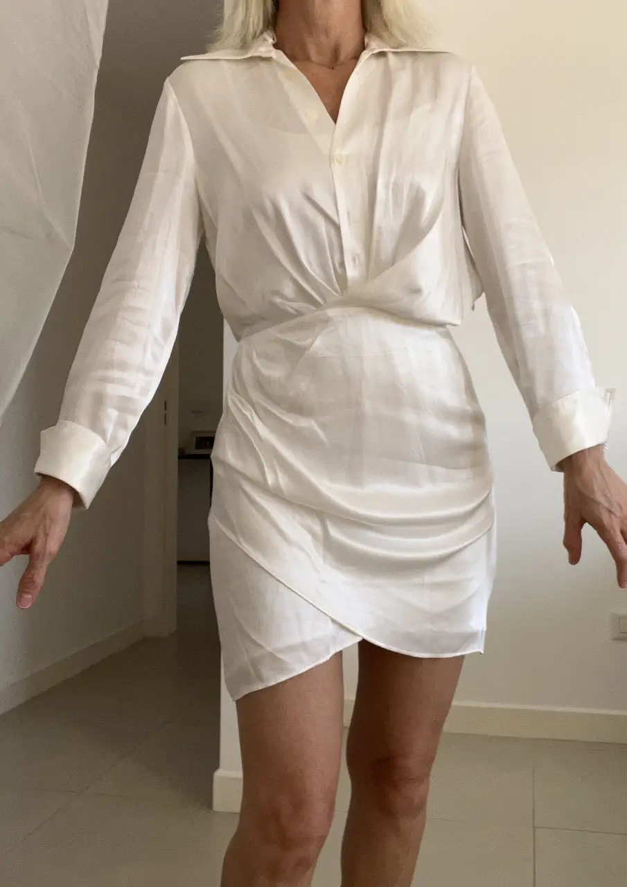 Vestido mini blanco de satén con diseño de camisa. Cuello camisero, mangas largas con puños y detalle fruncido en la cintura. Ideal para un look elegante y moderno.