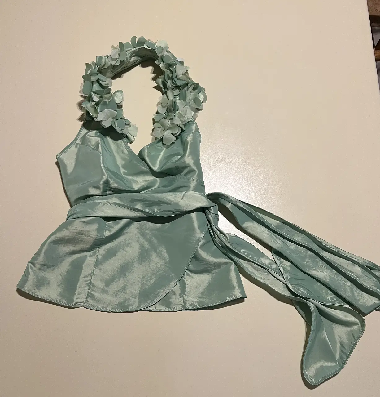 Top de fiesta verde agua con detalle de flores en el cuello y cinturón para atar. espalda abierta. Ideal para eventos especiales.