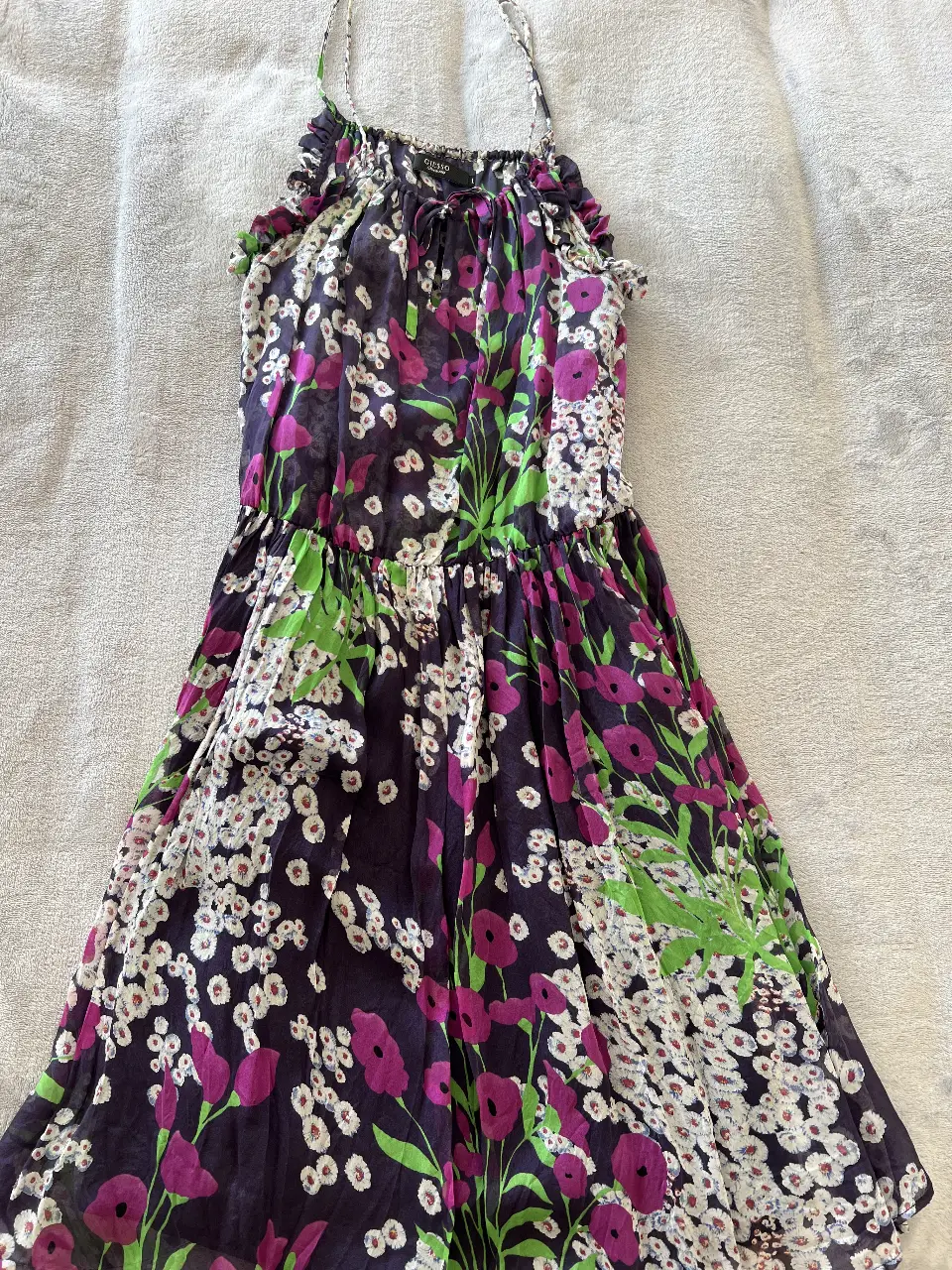 Vestido a la rodilla de mujer con estampado floral en tonos violetas, blancos y verdes. Diseño con tirantes finos, cintura elastizada y detalle de lazo en el escote. Ideal para un look fresco y femenino.