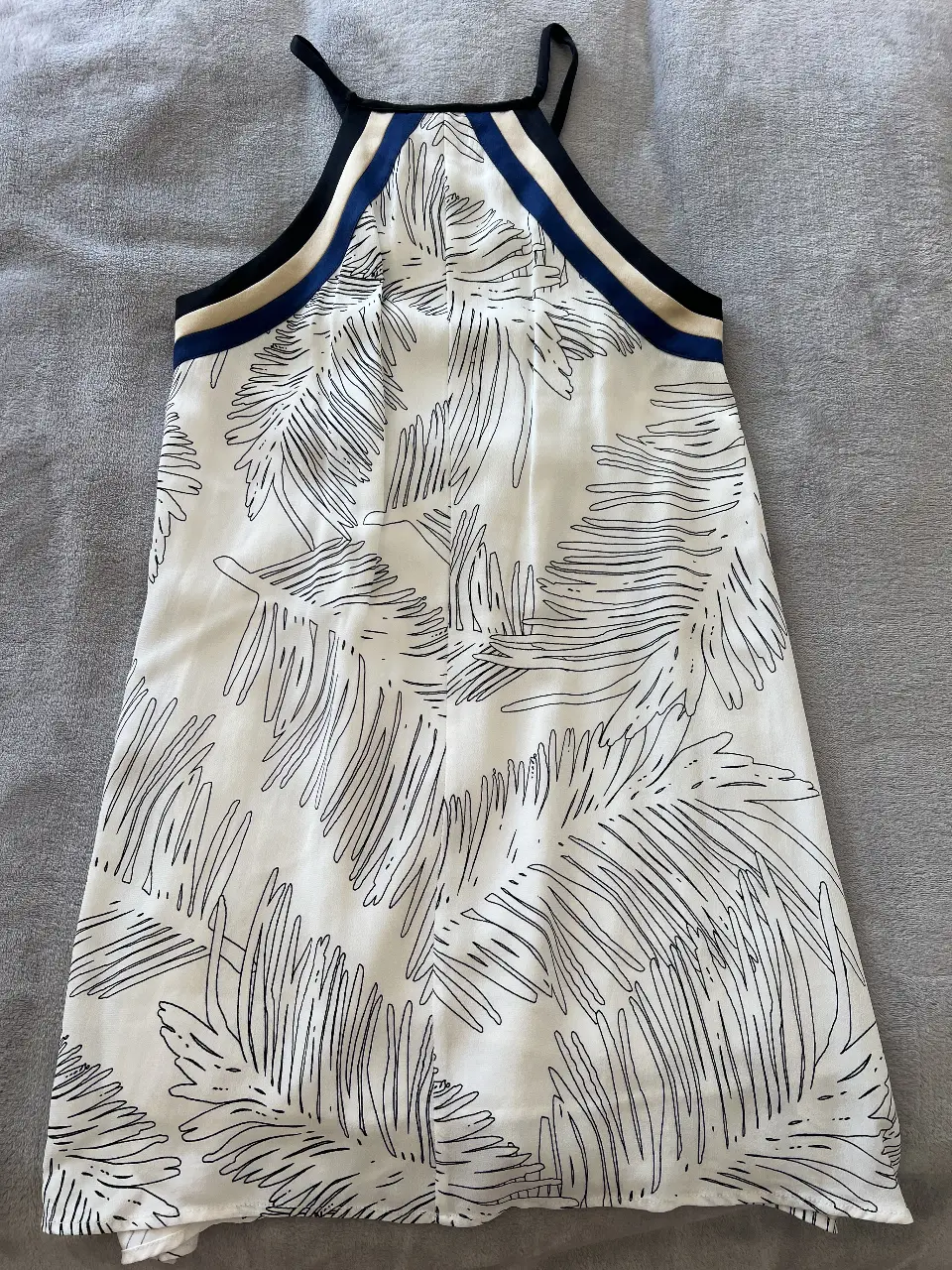 Vestido mini blanco con estampado de hojas negras. Cuello halter con detalles en negro y azul. Ideal para el verano.
