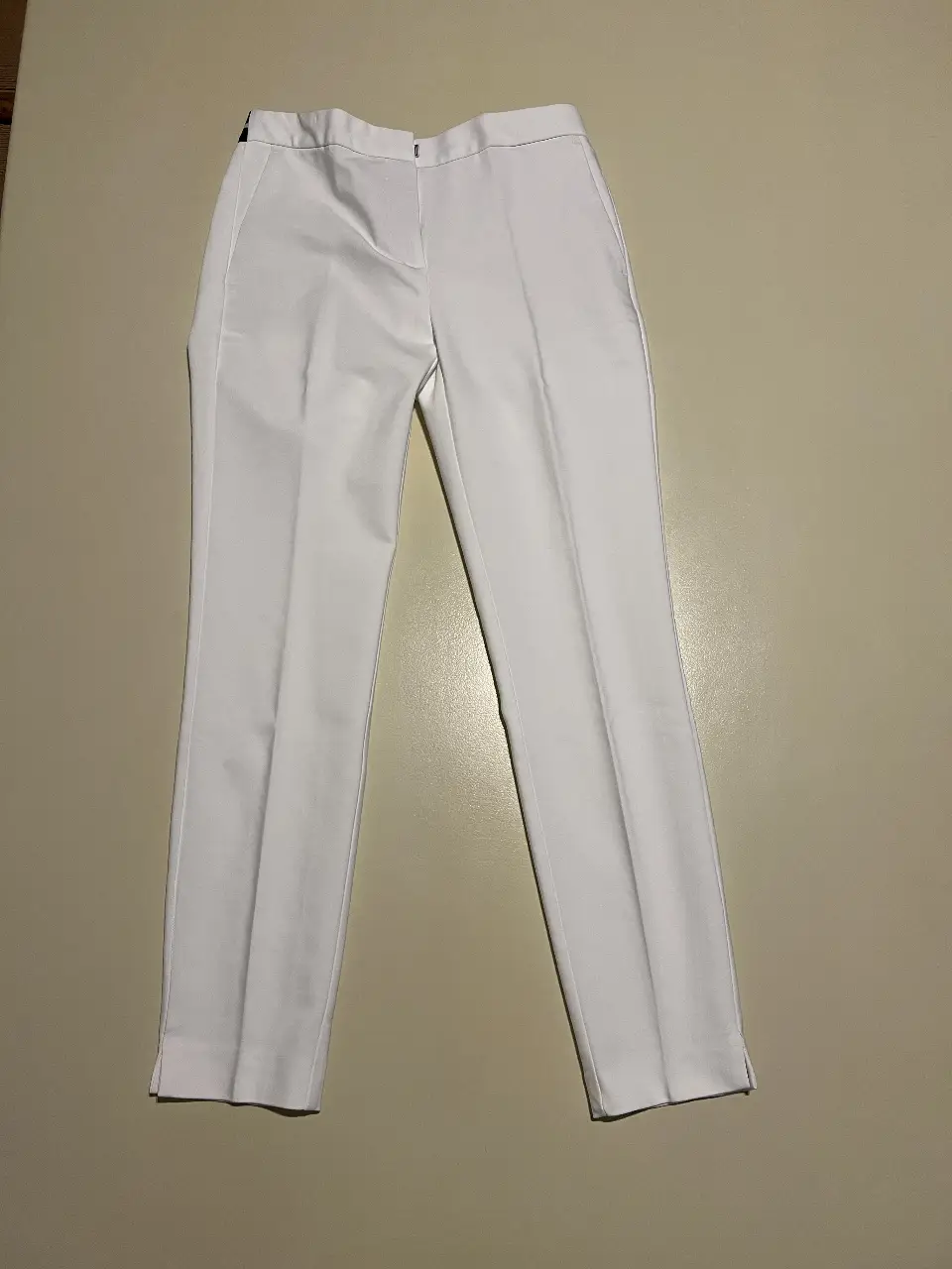 Pantalón sastrero blanco de mujer, tiro medio, con bolsillos laterales y cierre. Ideal para un look elegante y versátil.