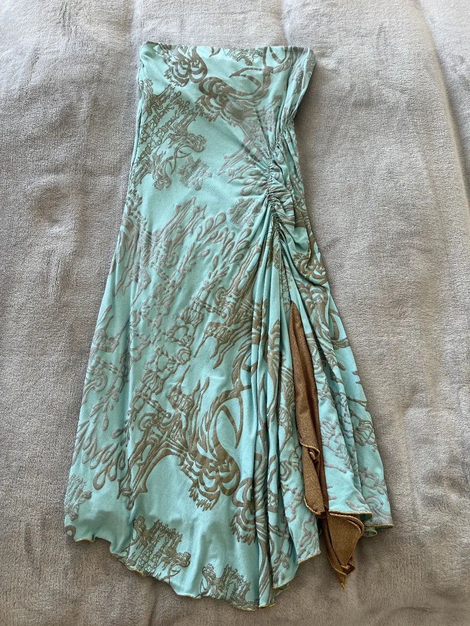 Vestido midi strapless de Victoria Keen, con estampado floral en tonos celeste y dorado. Diseño drapeado en un lateral y detalle de abertura. Ideal para una fiesta o salida.
