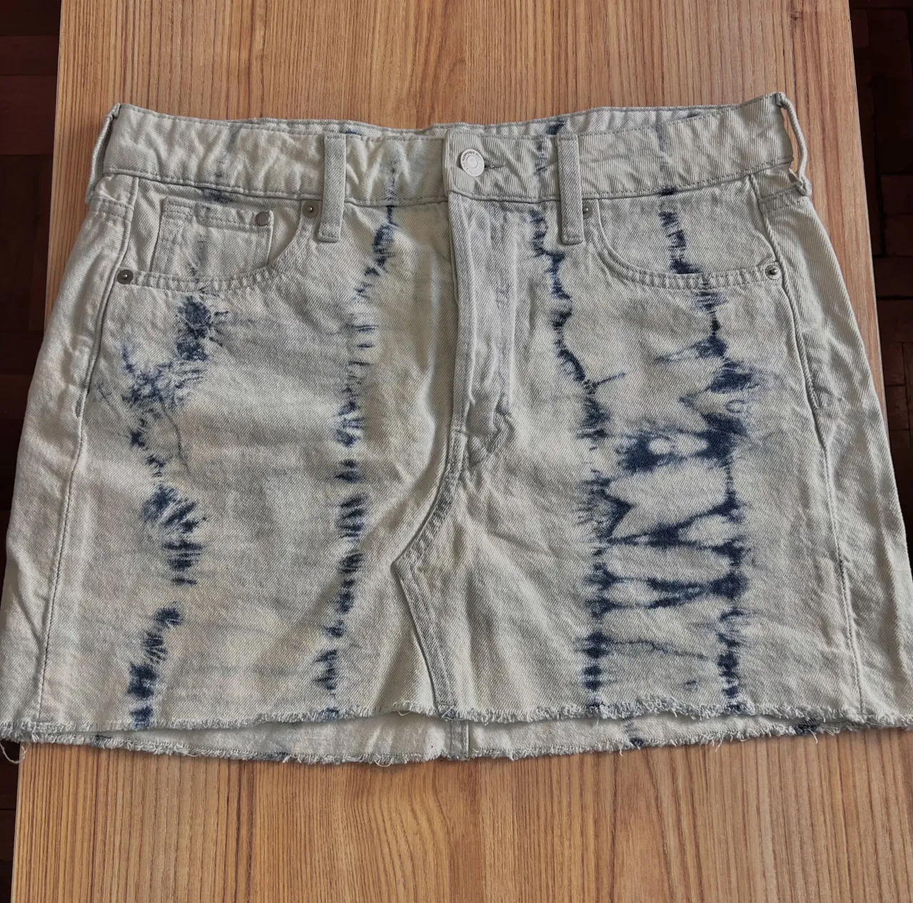 Pollera de jean corta con efecto tie-dye en tonos claros y azul. Tiene roturas deshilachadas en el borde inferior.