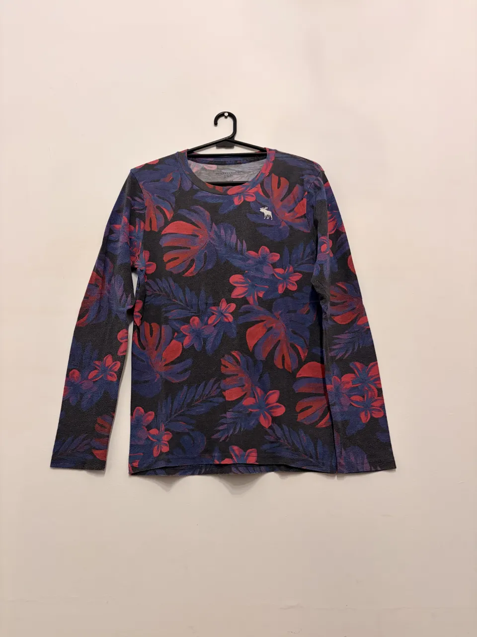 Remera Abercrombie Kids talle 13/14 de manga larga con estampa floral vibrante en tonos rojos y azules sobre fondo oscuro. Ideal para un look casual y descontracturado.