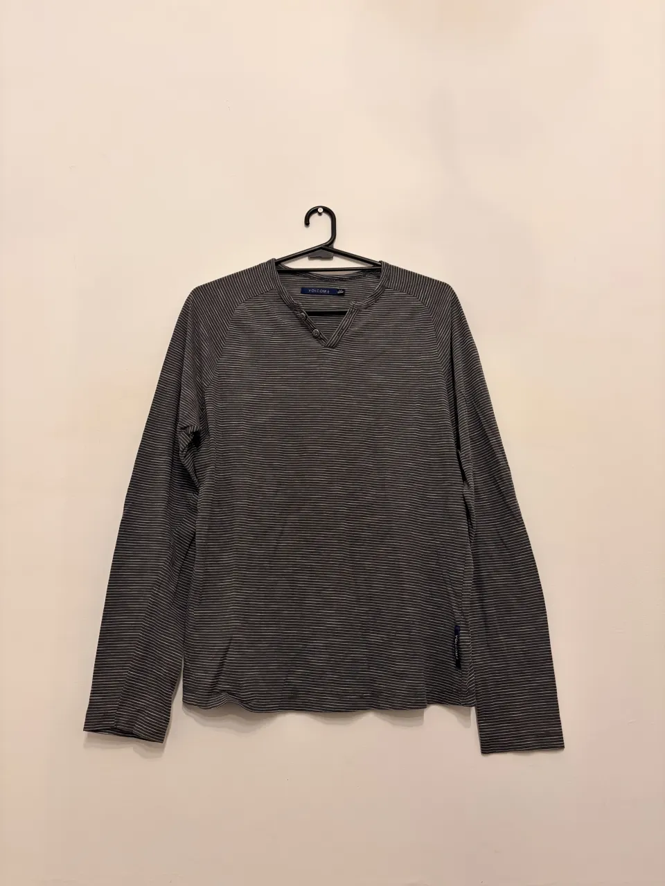 Remera manga larga de hombre, con finas rayas horizontales en gris y blanco. Cuello escote en V con dos botones.