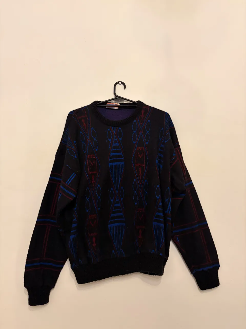Sweater de lanilla con un estampado geométrico en tonos azules y rojos sobre fondo negro. Diseño retro ideal para un look casual y abrigado.