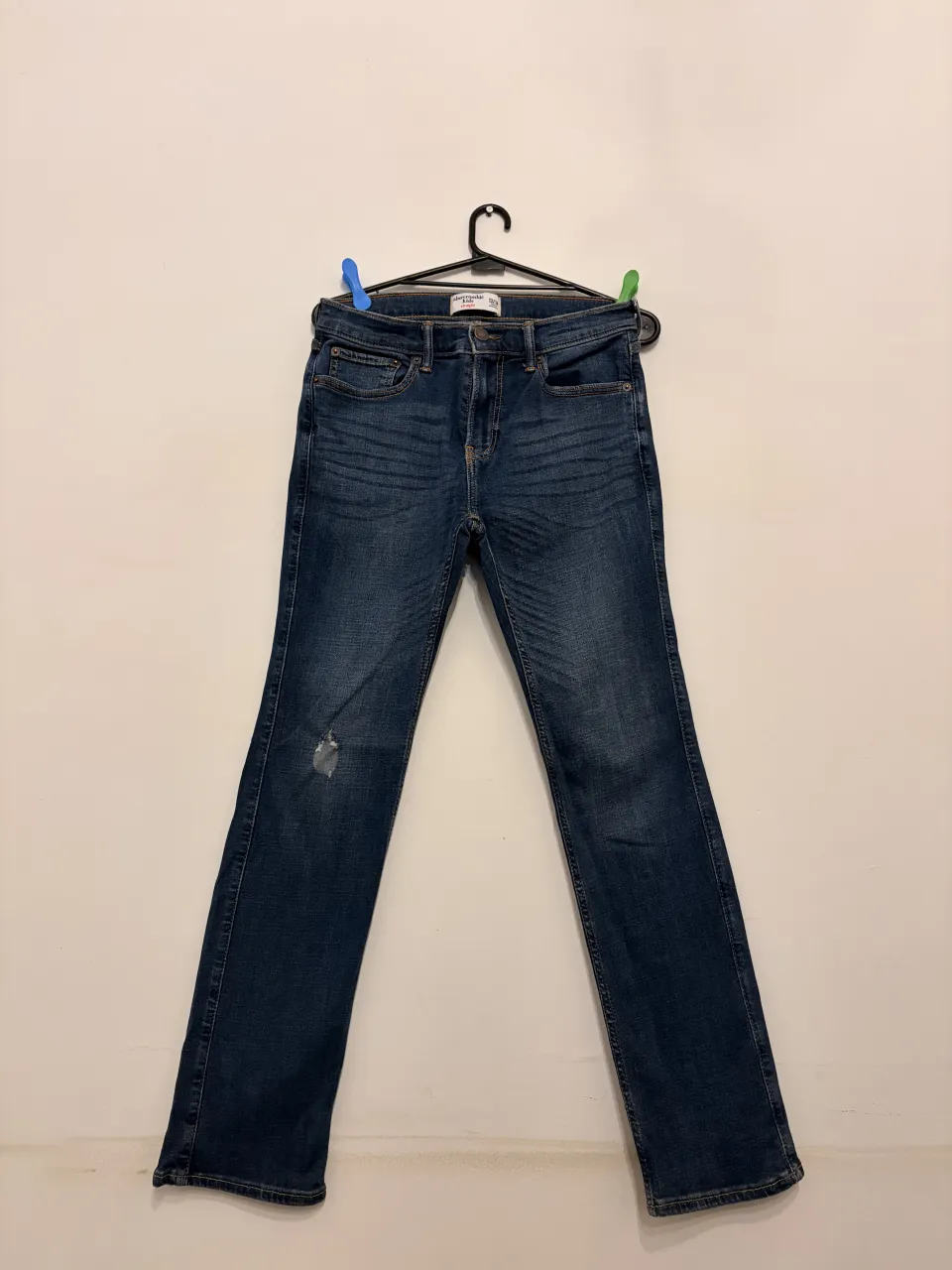 Jeans Abercrombie Kids talle 13/14 de corte recto, color azul oscuro, con un detalle de rotura sutil en la rodilla. Perfectos para un look casual y moderno.