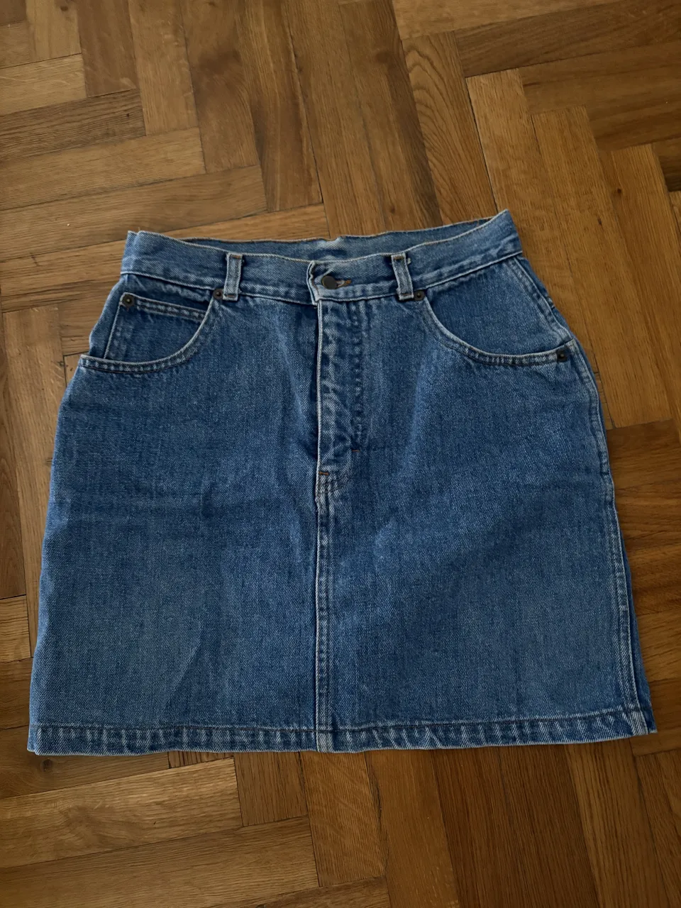 Pollera de jean azul, con bolsillos delanteros y traseros. Cierre y botón en la parte delantera.