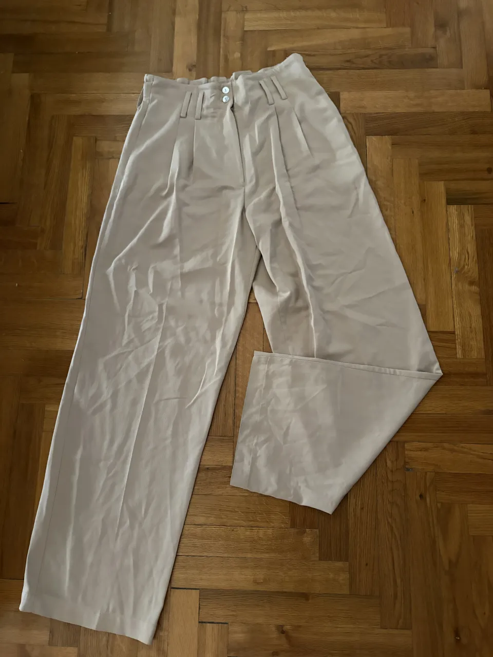 Pantalón de vestir color beige con dos botones en la cintura y cierre.