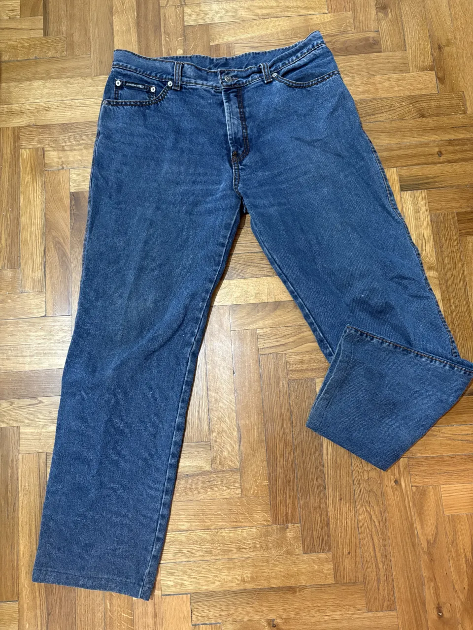 Jeans de corte clásico, color azul. Presentan bolsillos delanteros y traseros. La etiqueta trasera indica la marca.