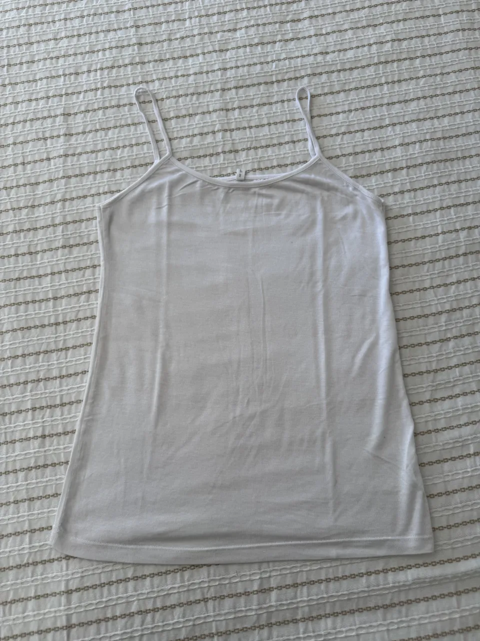 Musculosa blanca de breteles finos. Tiene un detalle metálico en el escote.