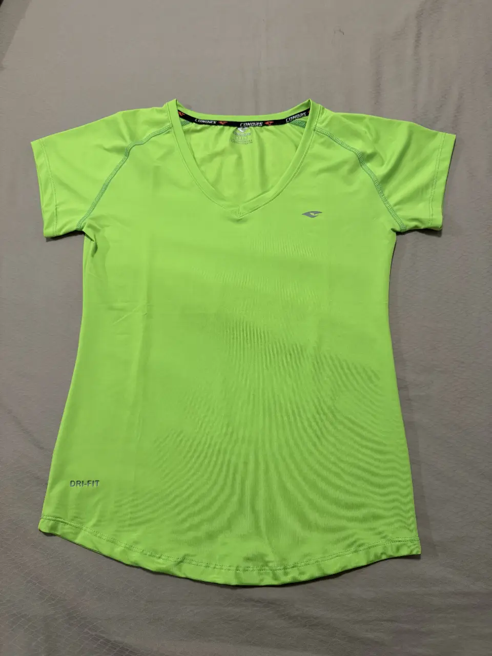 Remera deportiva Conors Dri-Fit SIN USO de mujer, color verde lima, con cuello en V y logo de la marca. Ideal para actividades físicas. Medidas: Sisa 44 cm, Cintura 40 cm, Cadera 43 cm, Largo 60 cm