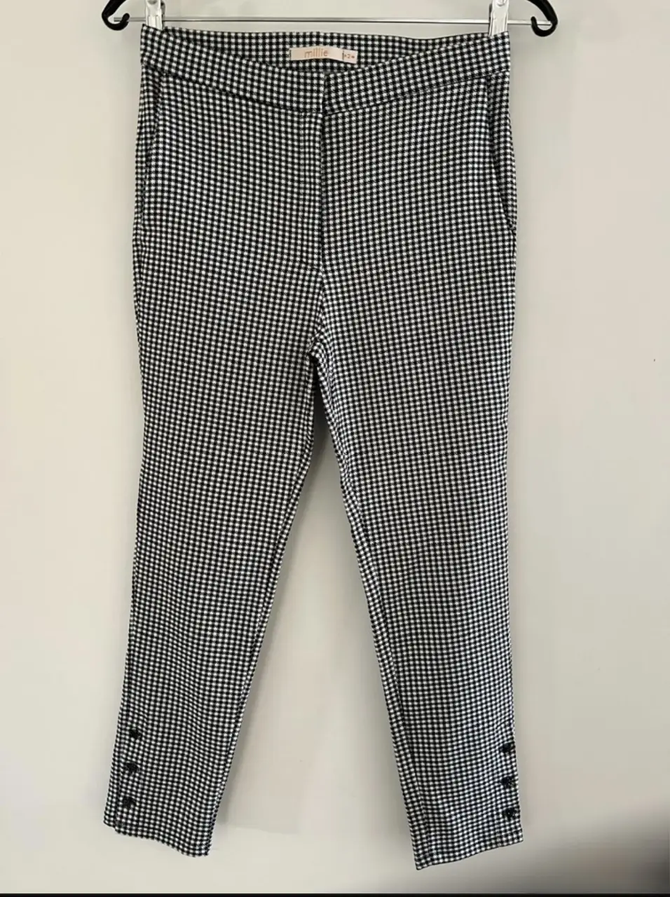 Pantalón sastrero de mujer con estampado de cuadros vichy en blanco y negro. Diseño clásico con corte recto y botones decorativos en los tobillos. Ideal para un look elegante y versátil.