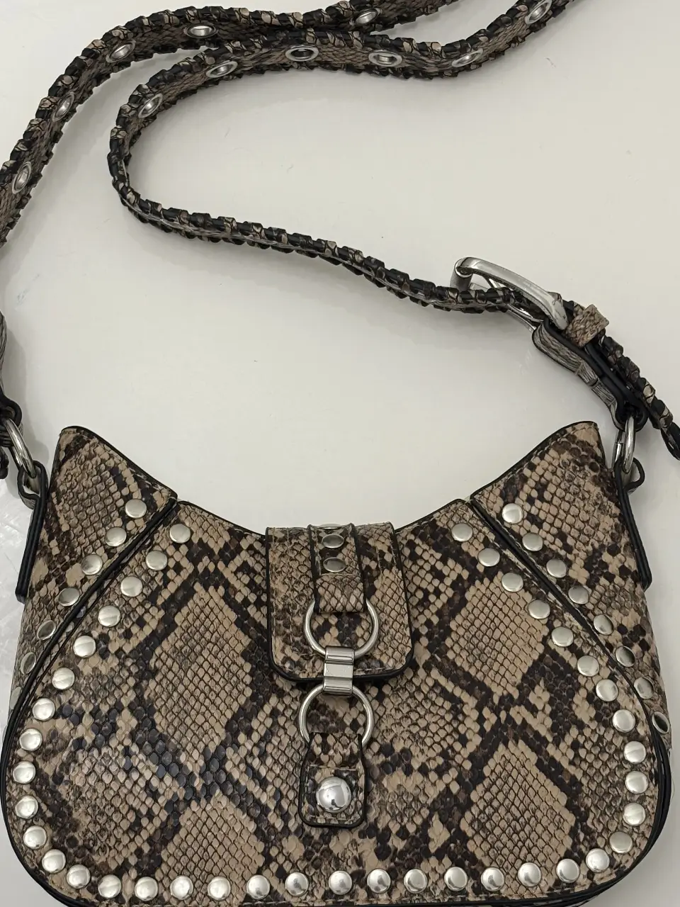 Cartera urban outfitter, bandolera con estampado de serpiente y tachas plateadas. Ideal para un look rockero y canchero. Cuenta con correa ajustable y cierre con hebilla.