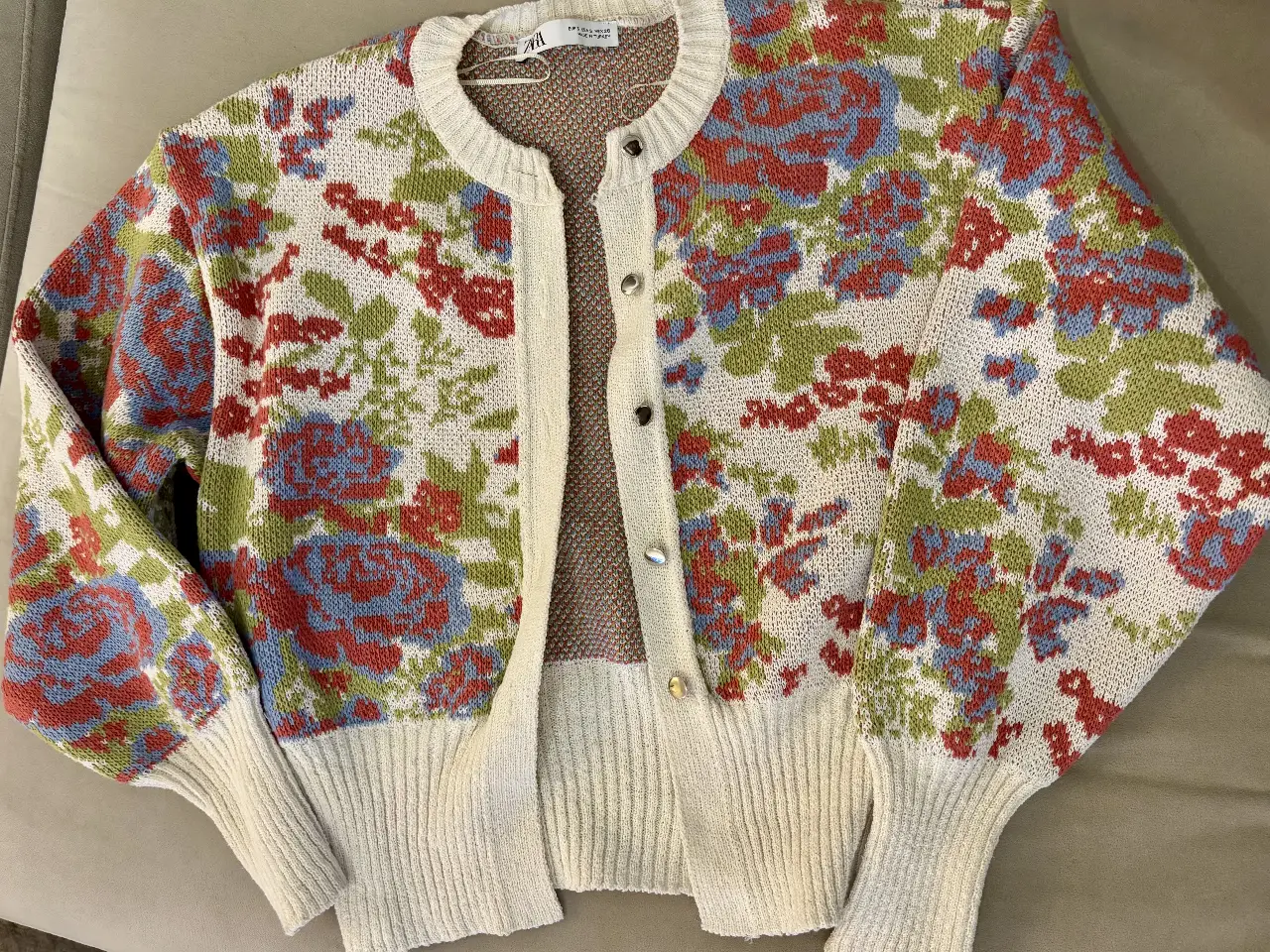 Cardigan de tejido con estampado floral en tonos rojos, verdes y azules sobre fondo blanco. Cuello redondo y botones. Ideal para un look vintage y femenino.