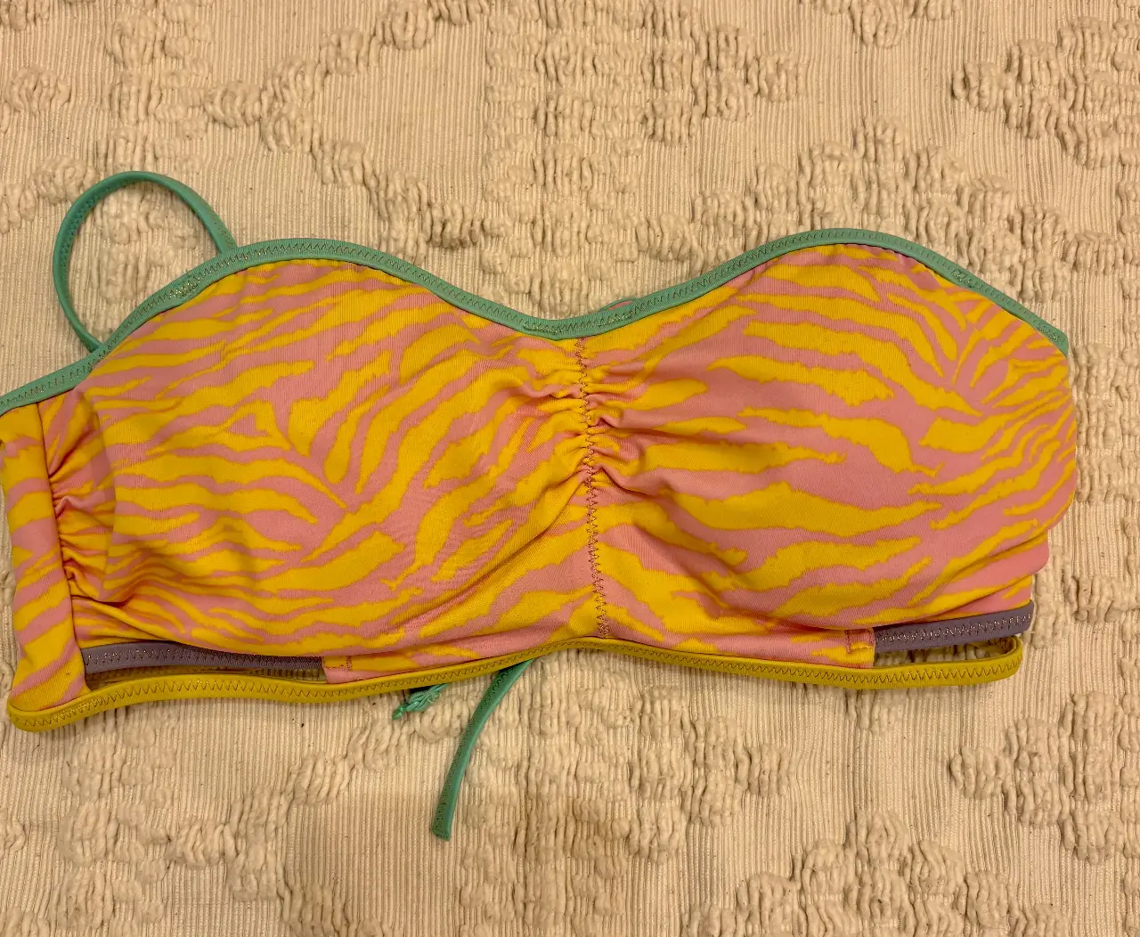 Top de bikini con estampado de cebra en tonos amarillo y rosa. Diseño bandeau con fruncido central y tirantes ajustables. Marca Victoria's Secret.