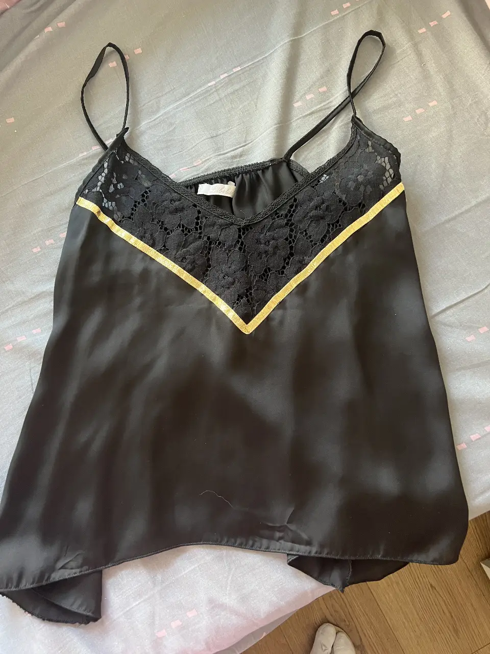 Top negro de satén con detalles de encaje y cinta dorada. Ideal para una salida o fiesta.