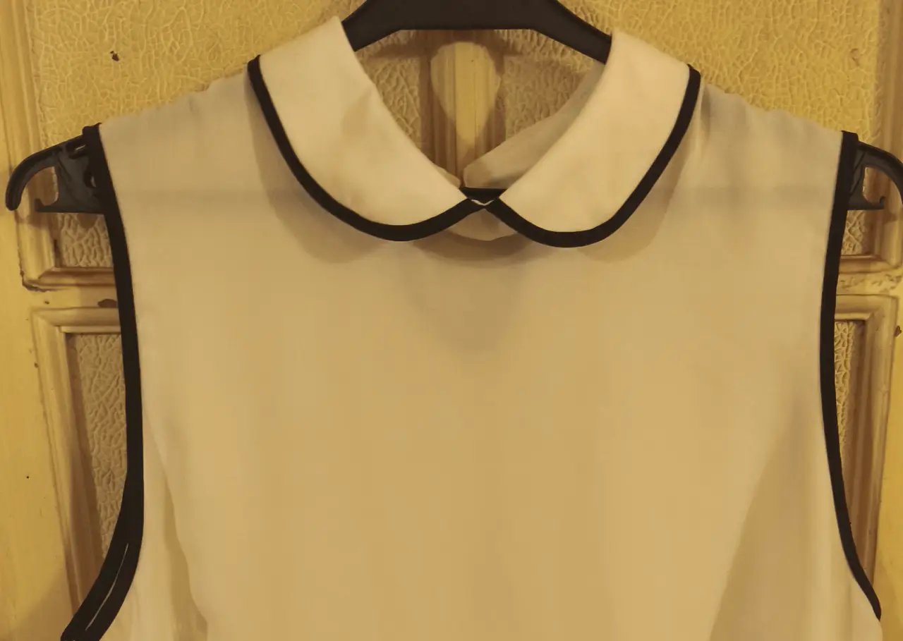 Blusa de mujer sin mangas, color blanco con detalles en negro en el cuello y bordes. Ideal para un look elegante y fresco.