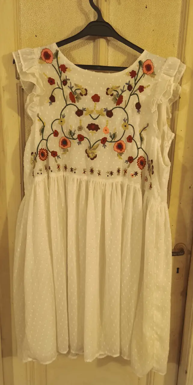 Vestido midi blanco con bordado floral en el pecho. Diseño con volados en las mangas y falda con caída.