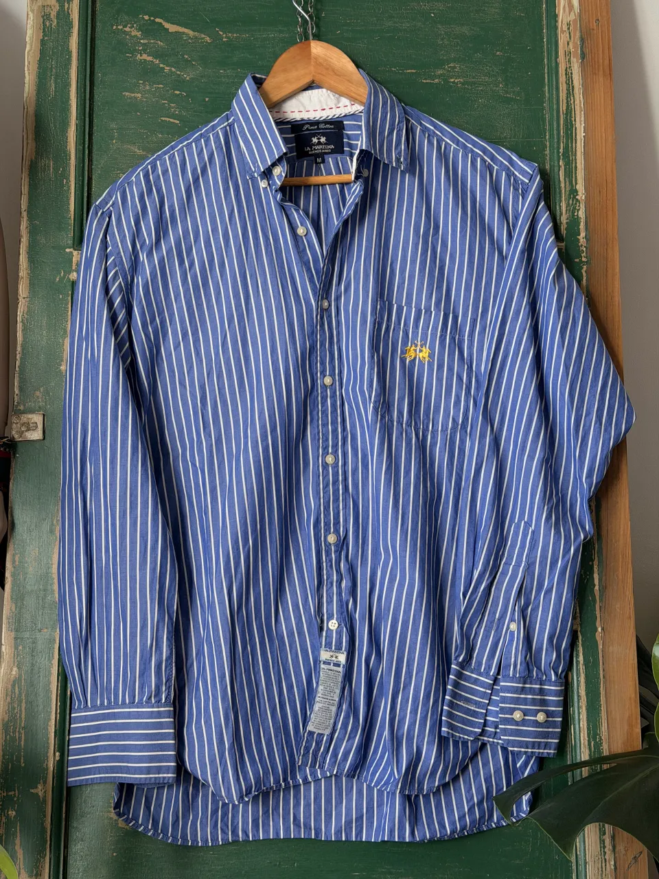 Camisa de vestir de hombre, manga larga, con un clásico diseño de rayas verticales azules y blancas. Presenta un bordado distintivo de dos jinetes en color amarillo en el bolsillo del pecho, un detalle que le da un toque de elegancia y exclusividad. Perfecta para un look casual o semi-formal.