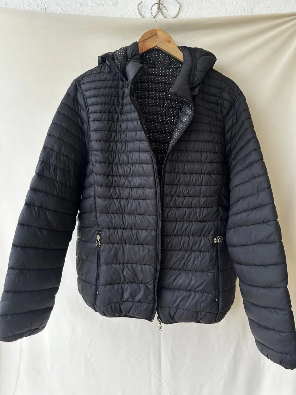 Campera negra acolchada con capucha. Posee forro interior con estampa de lunares blancos sobre fondo negro. Tiene cierre al frente y bolsillos laterales con cierre.