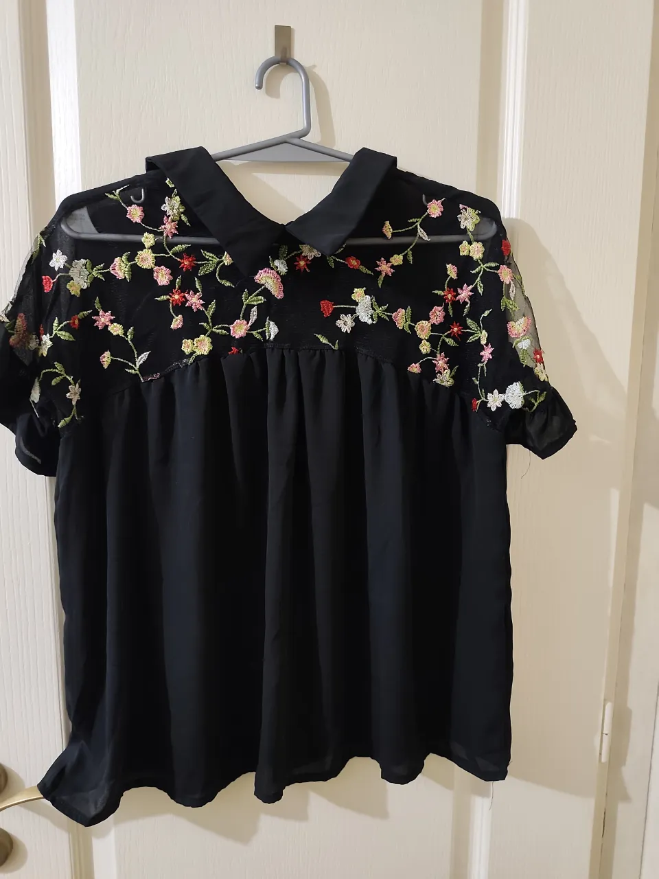 Blusa negra con cuello y mangas cortas. Presenta bordados florales de colores en la parte superior y las mangas. La espalda tiene un lazo. sin etiqueta. la tela es tipo gasa 
