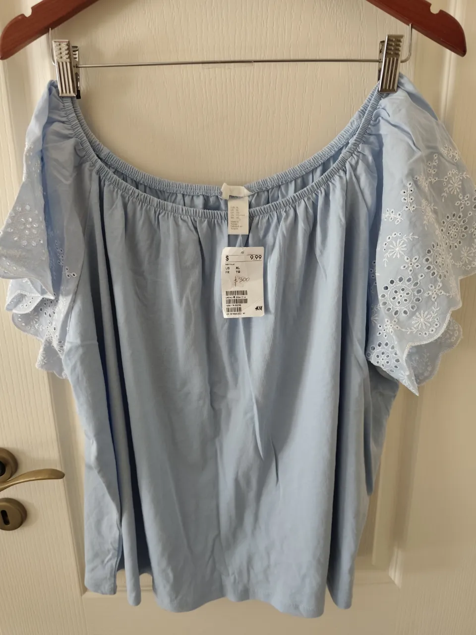 Blusa celeste de mangas cortas con bordados blancos en las mangas. Escote elástico con volados.