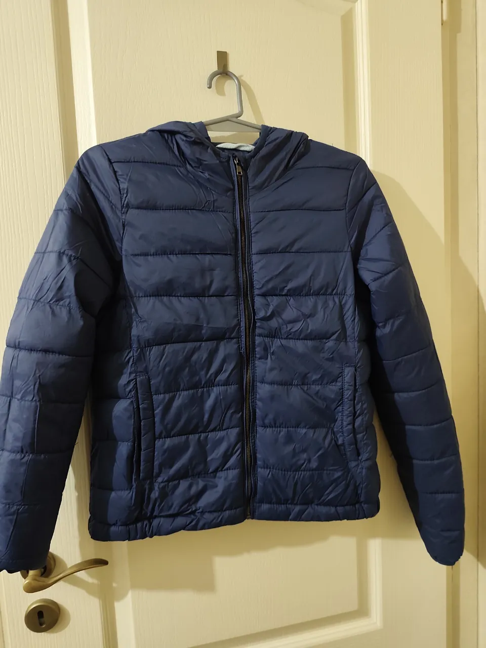 Campera azul acolchada con capucha y cierre al frente. Bolsillos laterales.