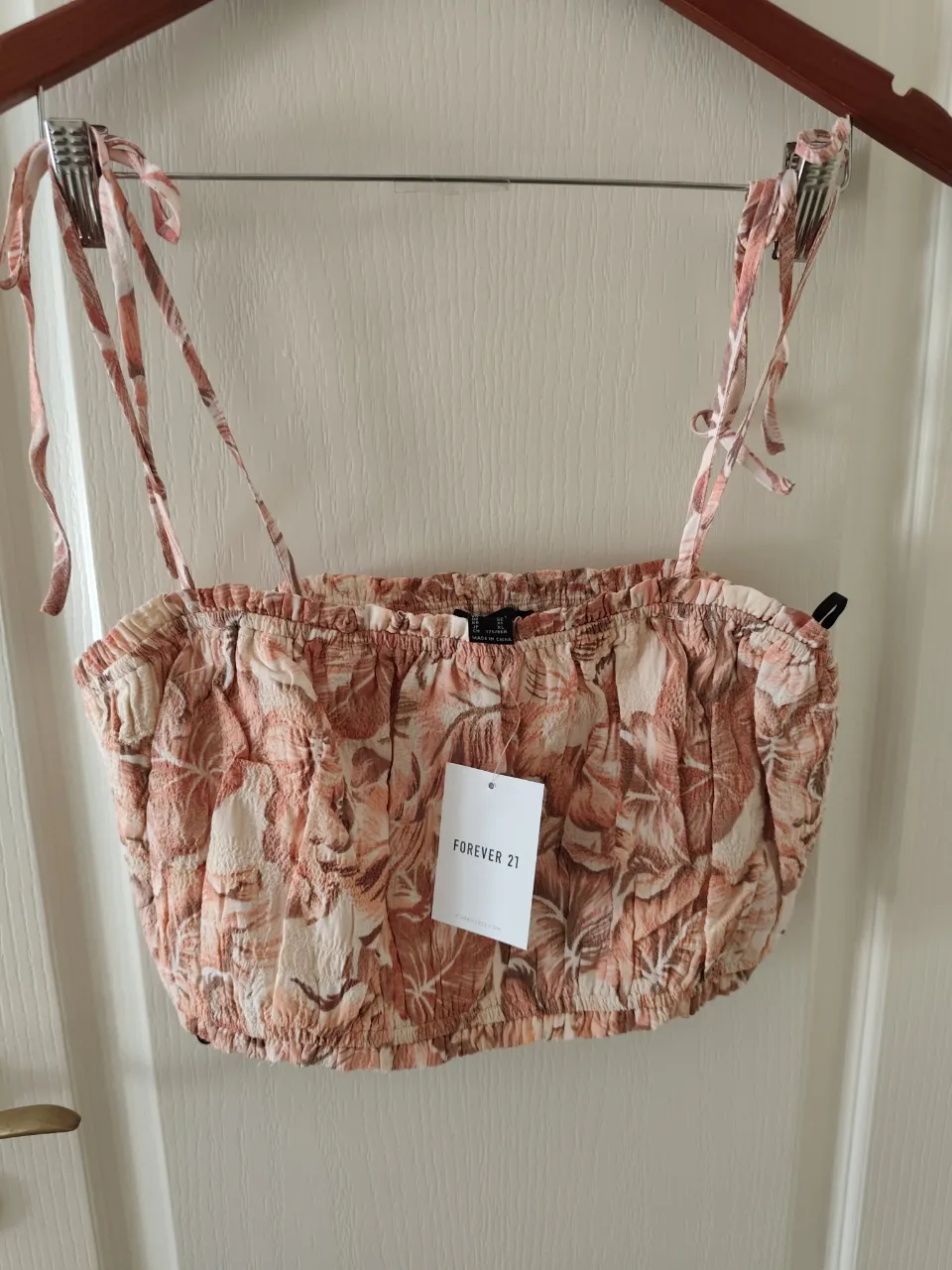 Top corto con estampado floral en tonos coral y blanco. Posee tiras finas regulables con lazo en los hombros y elástico en el borde superior e inferior.