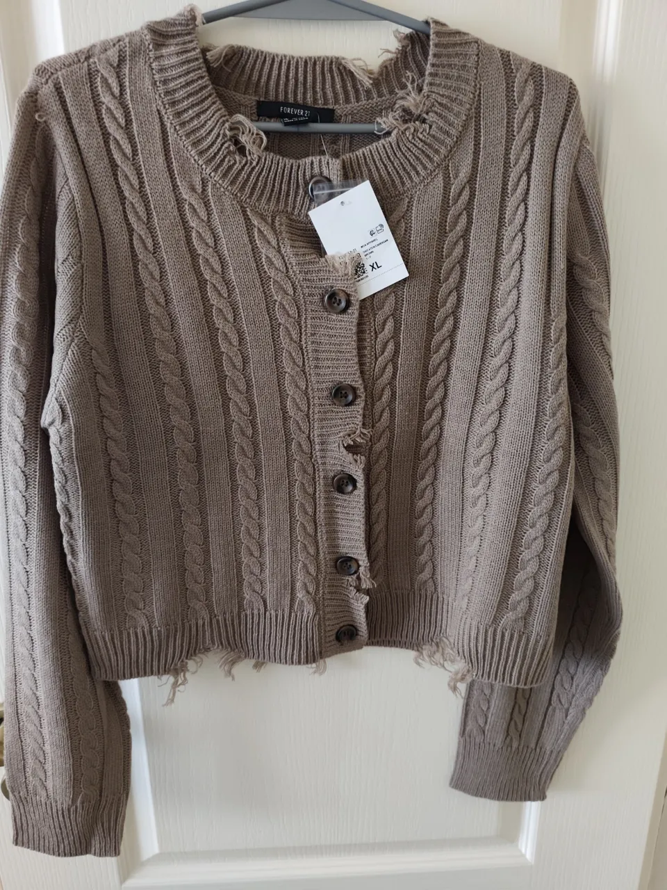 Cardigan de tejido de punto con botones al frente y detalles deshilachados en cuello y puños. Posee trenzas tejidas en toda la prenda.