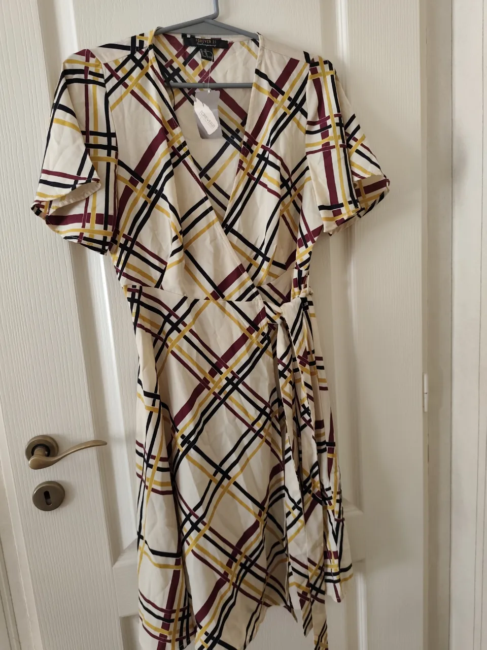 Vestido cruzado con estampado de cuadros en tonos blanco, amarillo, negro y bordó. Posee mangas cortas con volados y lazo para atar a un costado.