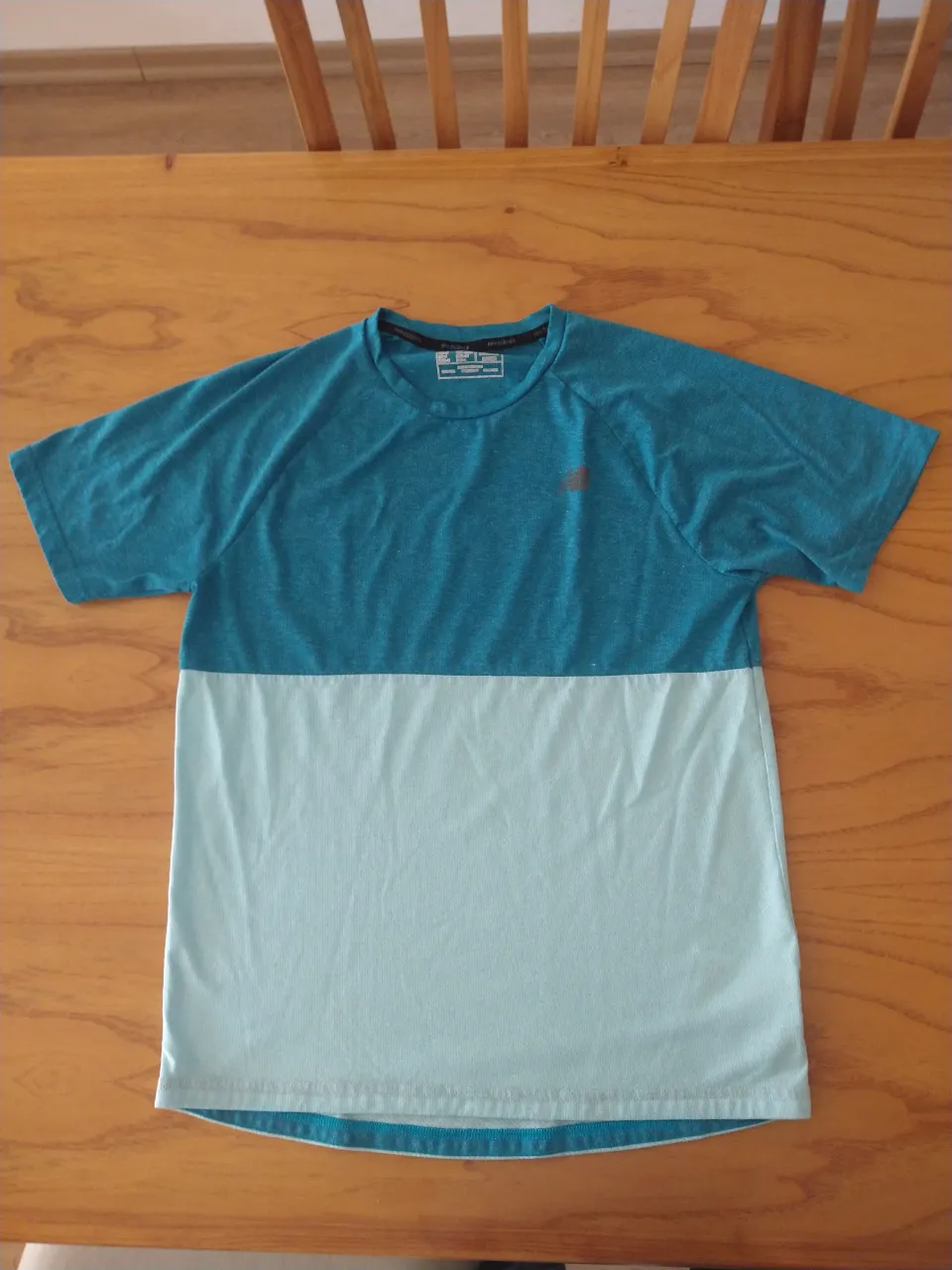 Remera deportiva de manga corta, con cuello redondo. Diseño de dos bloques de color: la parte superior es azul verdoso y la parte inferior es celeste claro.