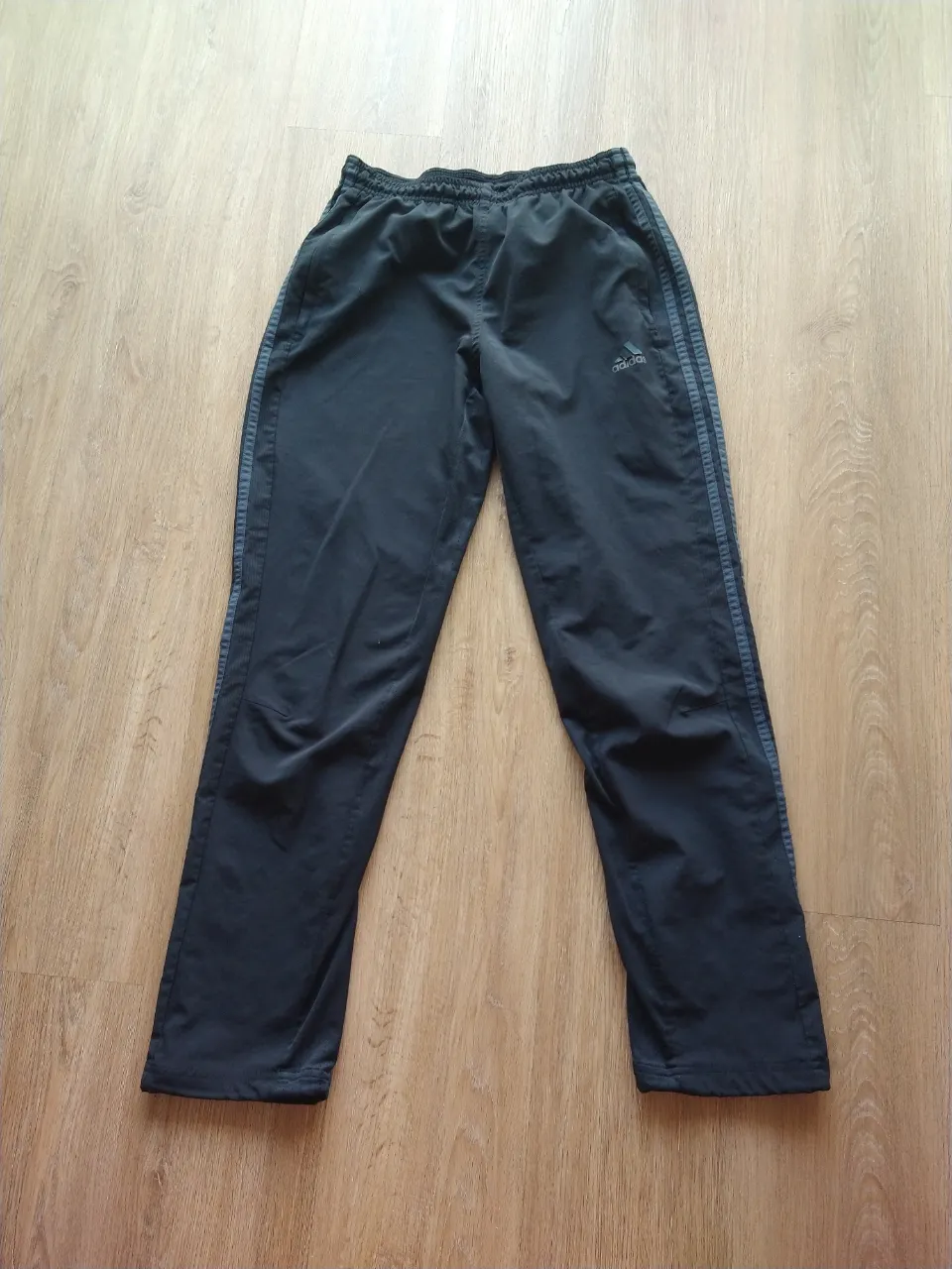 Pantalón deportivo negro con tres franjas grises a los costados. Posee cordón ajustable en la cintura.